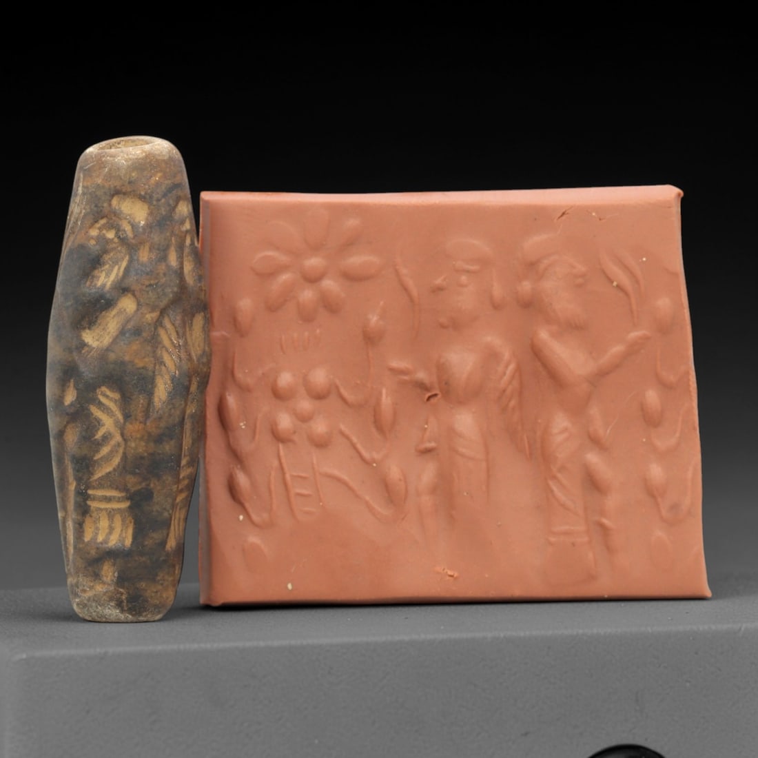 Ancient Steatite Cylinder Seal - Mesopotamian Figural & Botanical Scene, 85ZR: Carved from dense steatite, this ancient Mesopotamian cylinder seal features a precise linear relief composition of two human figures interacting with floral and botanical motifs, executed in the char