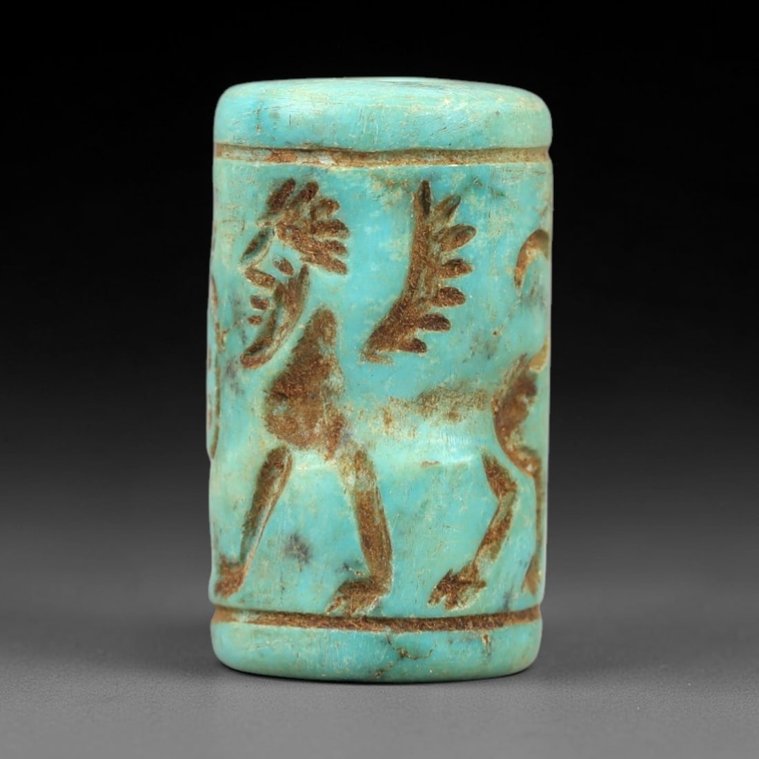 Ancient Turquoise Cylinder Seal - Near Eastern Ritual Artifact, 50AN: Carved from turquoise, this cylinder seal features intricate relief carvings of a winged quadrupedal creature (likely a griffin or protective spirit) and accompanying symbolic motifs, encircled by hor