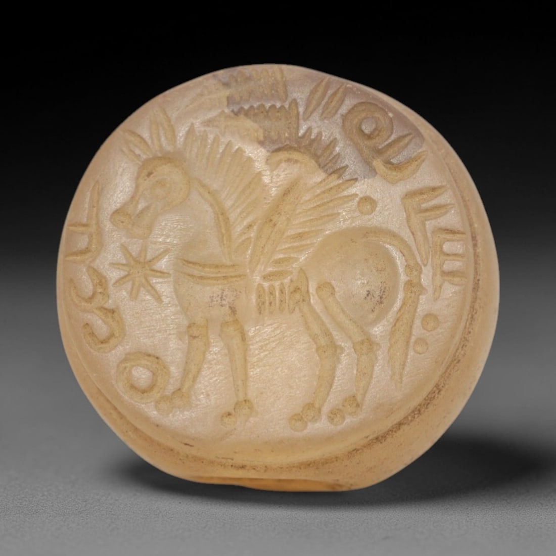 Ancient Chalcedony Hemispherical Stamp Seal - Near Eastern Winged Horse & Script, 30ZP: Crafted from translucent, pale chalcedony, this hemispherical stamp seal bears a deeply incised depiction of a stylized winged horse, rendered in linear relief with detailed feathered wings, patterned