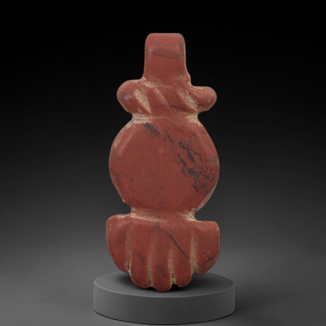 Ancient Stone Tyet Amulet - Egyptian Carved Pendant, 20AG: This amulet is carved from a dense red stone, likely red jasper, exhibiting a rich, earthy patina with subtle lighter inclusions and surface weathering. The form is a stylized Tyet (Knot of Isis) amul