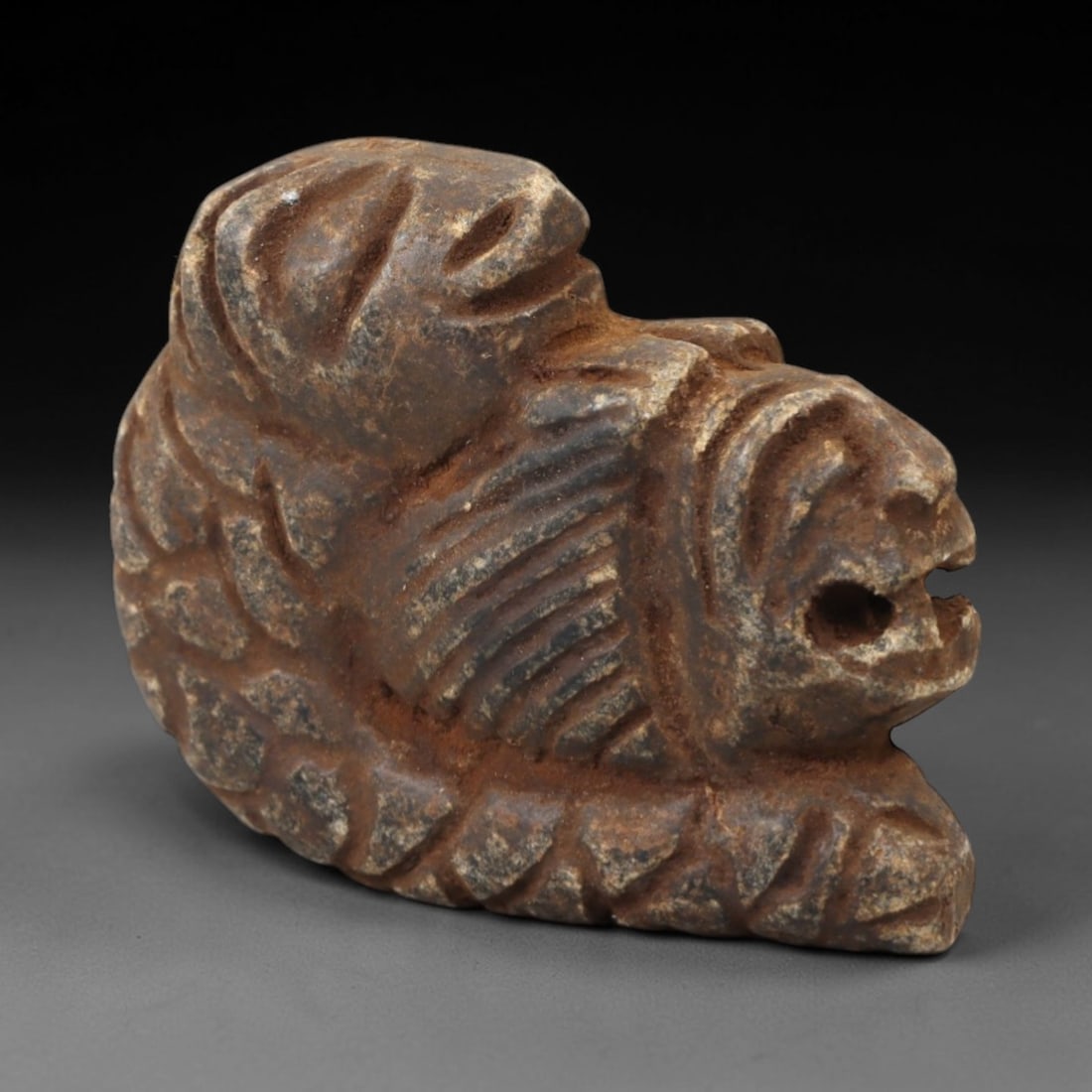Ancient Steatite Lion - Near Eastern Amulet Figurine, 97AK: Carved from steatite, this amulet depicts a recumbent lion with incised linear details defining the mane, facial features, and body, including a suspension hole in the muzzle for wearable use. Attribu