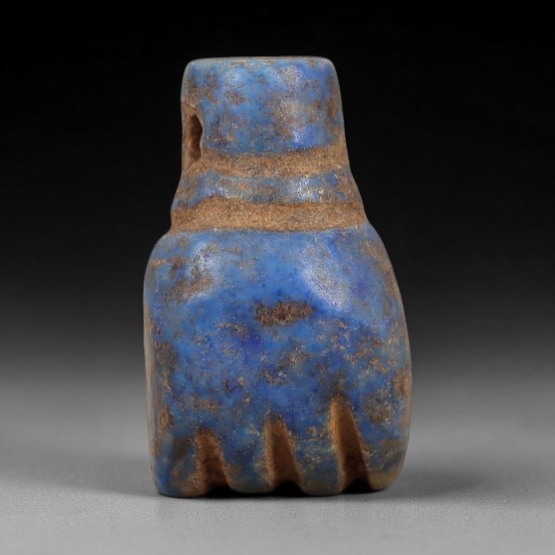 Ancient Lapis Lazuli Fist Amulet - Egyptian Ritual Pendant, 14AP: Carved from lapis lazuli, this amulet is formed in the shape of a clenched fist, with a cylindrical upper lug pierced for suspension, its body marked by two incised horizontal bands and a serrated low