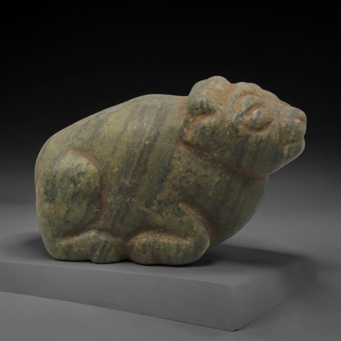 Ancient Stone Bovid - Near Eastern Amulet Figurine, 59XR: Carved from banded green stone, this amulet depicts a recumbent bovid in a stylized, compact form characteristic of Ancient Near Eastern craftsmanship. The animal is rendered with simplified anatomica