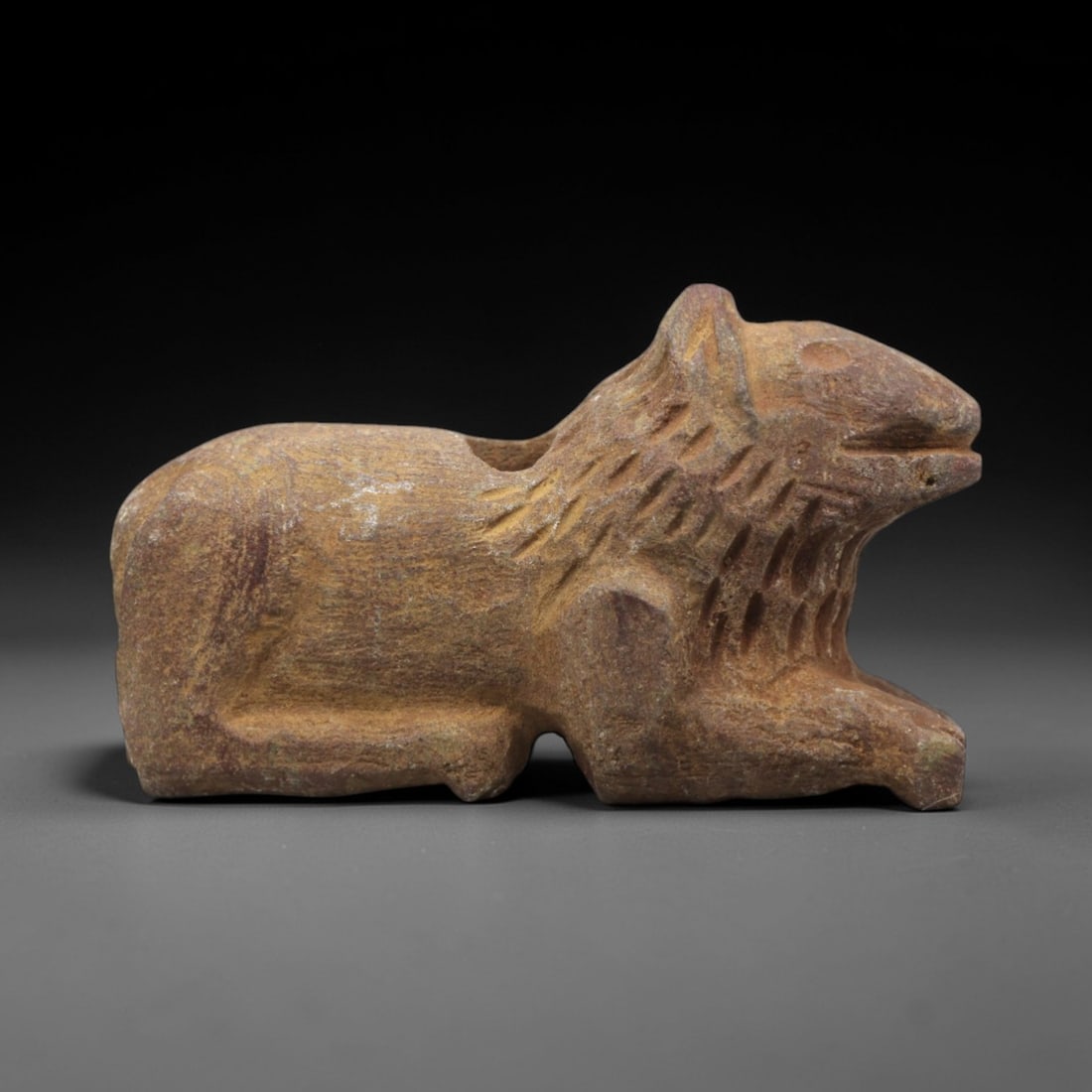 Ancient Stone Lion Amulet - Near Eastern Recumbent, 42ZR: Carved from warm tan-hued stone with a matte, weathered patina, executed in a stylized recumbent form characteristic of Near Eastern zoomorphic amulet craft. The figure depicts a lion in a resting pos