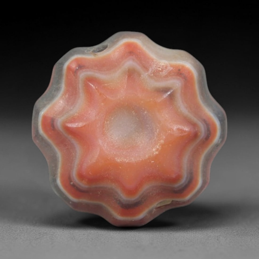 Antique Agate Star Bead - Central Asian Carved Gemstone, 19AR: Carved from banded agate with a soft greyish-white outer band and rich orange-red core, this bead features a symmetrical eight-pointed star form with layered, scalloped edges and a recessed central ca