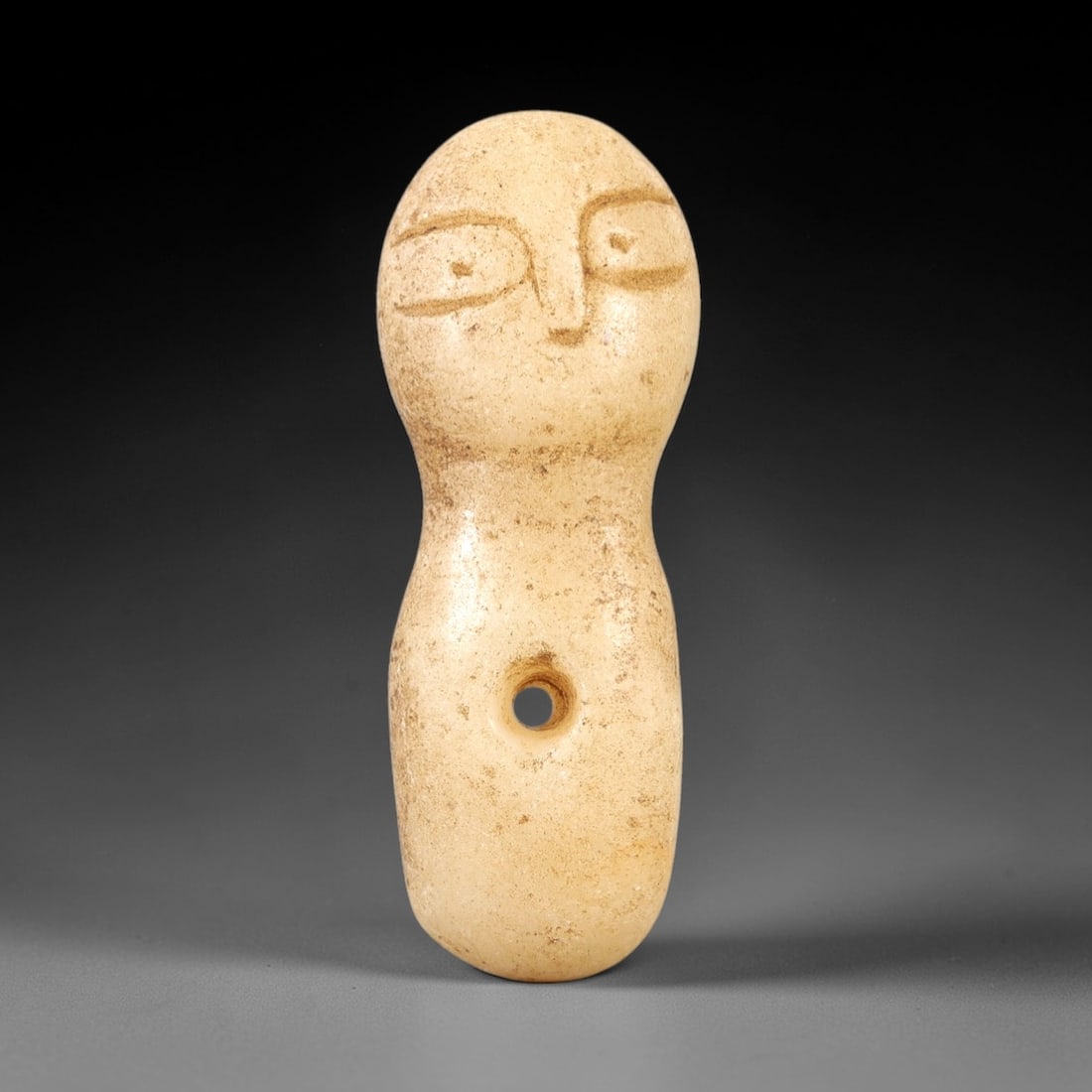 Ancient Stone Anthropomorphic Idol - Near Eastern Amulet, 6AL: Carved from pale tan stone, this anthropomorphic idol features a stylized rounded head with incised eyes, a simplified nose, and an elongated cylindrical body. A central perforation confirms its funct