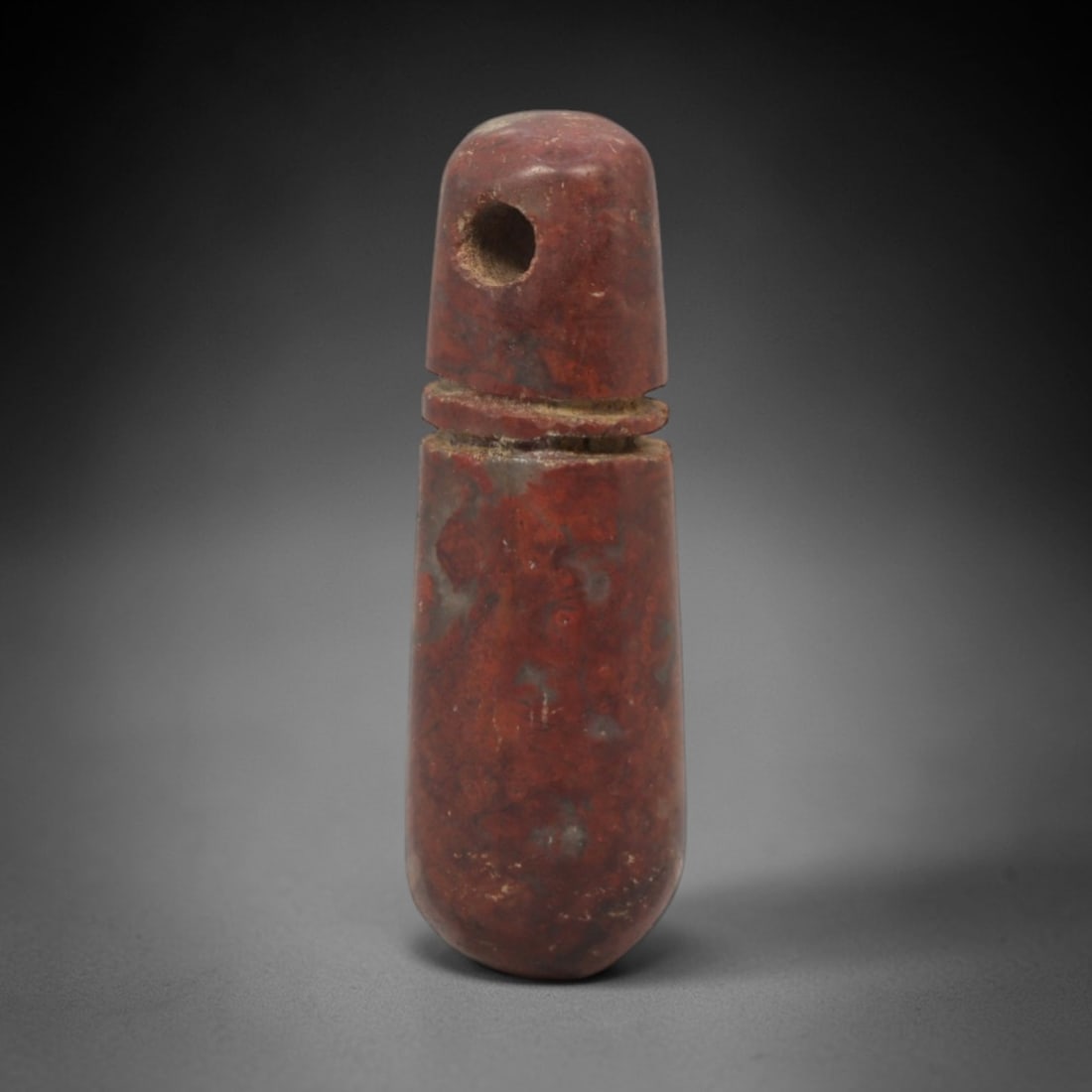 Ancient Stone Wadj Amulet - Egyptian Pendant, 53XQ: Carved from a rich reddish stone, this amulet takes an elongated, tapering form with a perforated domed top and a single incised horizontal collar, characteristic of the Egyptian wadj amulet typology