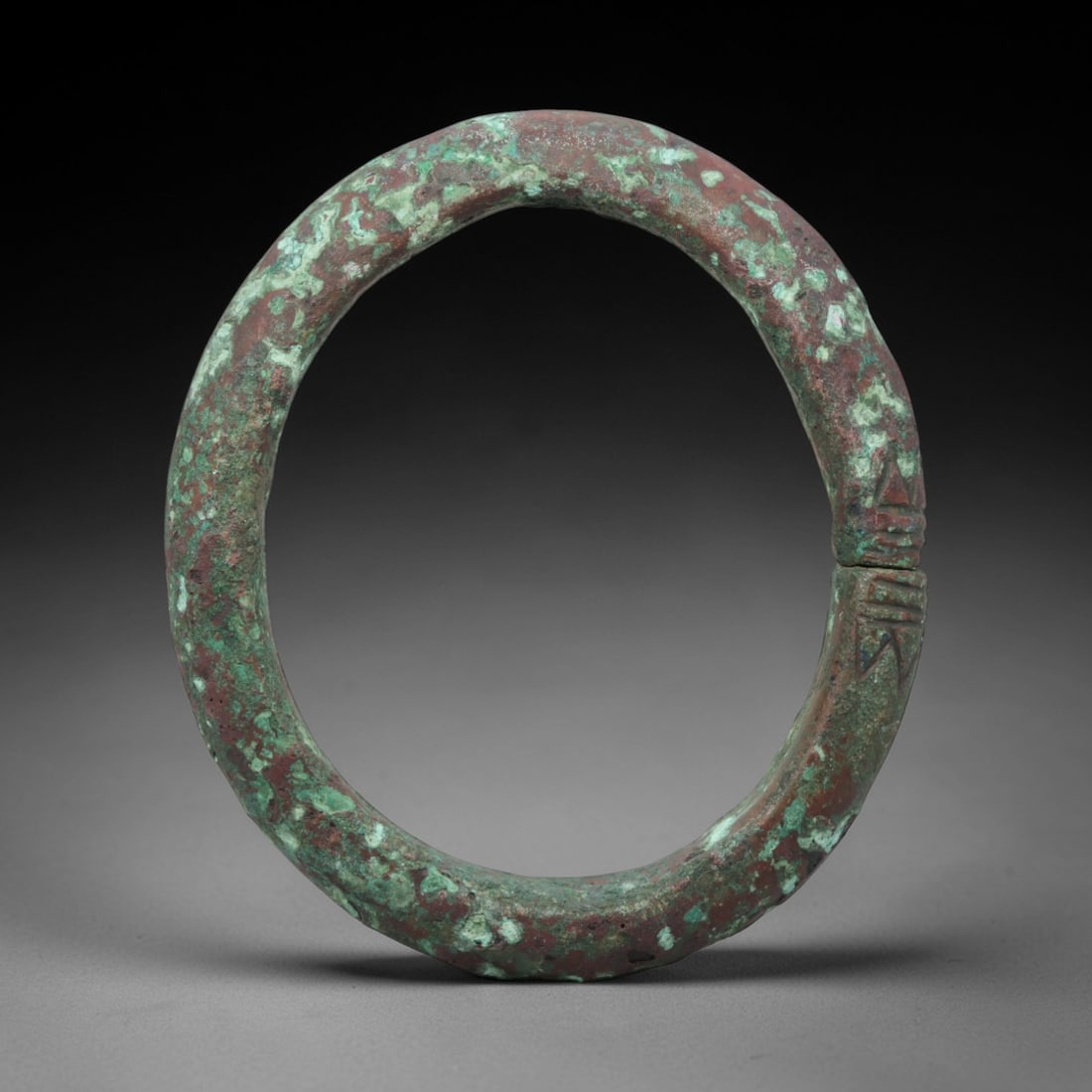 A Roman Bronze Bracelet, 1st-3rd Century CE, 98FT: Cast from bronze with a robust, fully rounded section, the bracelet is formed as a near-complete circle with a narrow terminal gap. One terminal features a series of shallow, vertical incised linear m