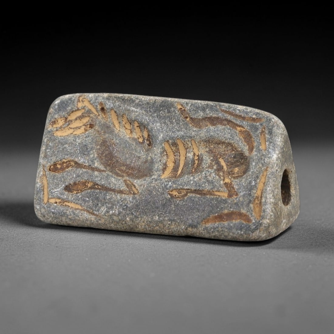 Ancient Stone Stamp Seal - Near Eastern Animal Figure, 50AM: This triangular stamp seal is carved from dark stone, featuring an incised intaglio depiction of a stylized animal form with linear detailing characteristic of ancient Near Eastern glyptic art. The se
