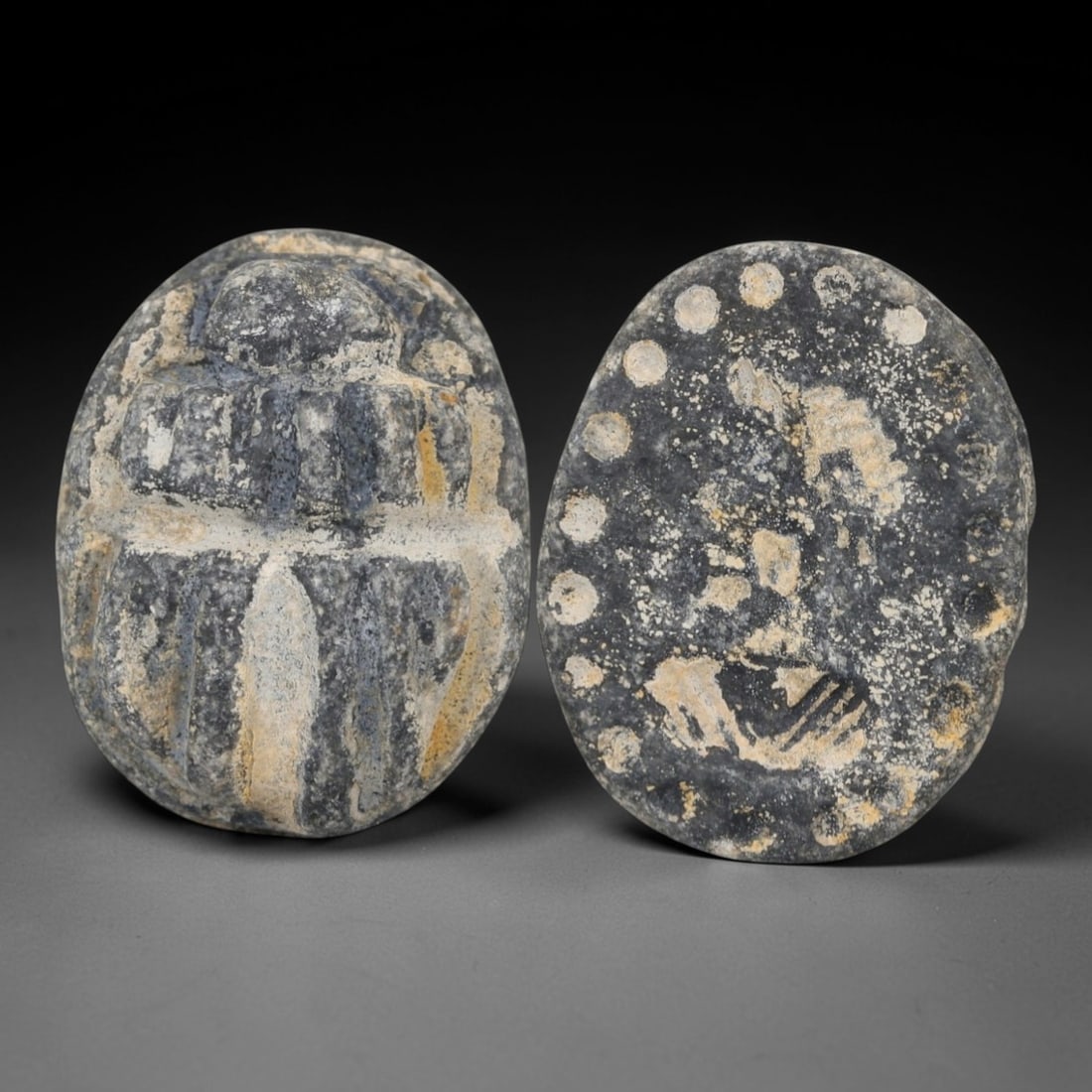 An Ancient Near Eastern Stone Scarab Stamp Seal with Noble Motif, 1st Millennium BCE, 94AC: Carved from dark, granular stone with natural surface patination and subtle tonal variation, the object is formed as an oval scarab seal. The dorsal side is modeled in low relief with a segmented cara