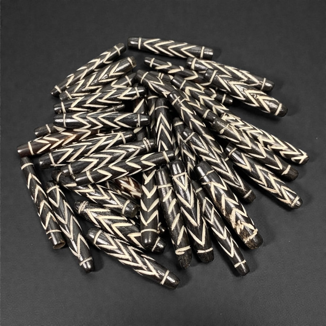A Tibetan Bone Bead Group, Inlaid Chevron Pattern, 20th Century, 72S: Composed of animal bone, each bead features an elongated cylindrical form with a tapered end, consistent in length and diameter across the group. The surface displays an inlaid chevron pattern, with w