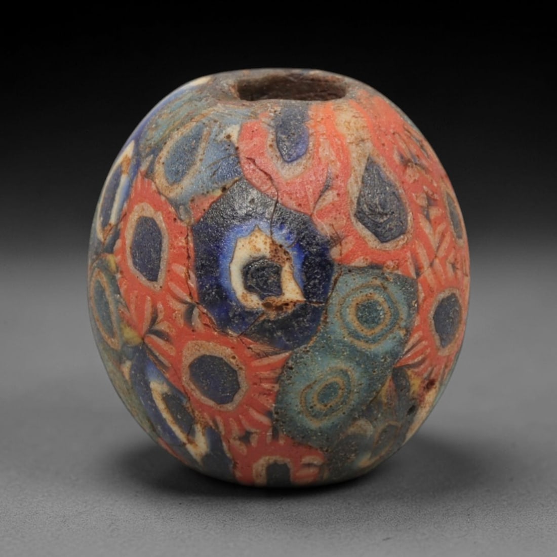 Ancient Glass Bead - Roman Egyptian Peacock Eye Amulet, 48ZN: Crafted from mosaic glass, this ovoid bead features a central suspension hole and is decorated with intricate peacock eye and floral motifs in red, blue, teal, and white glass inlay, characteristic of