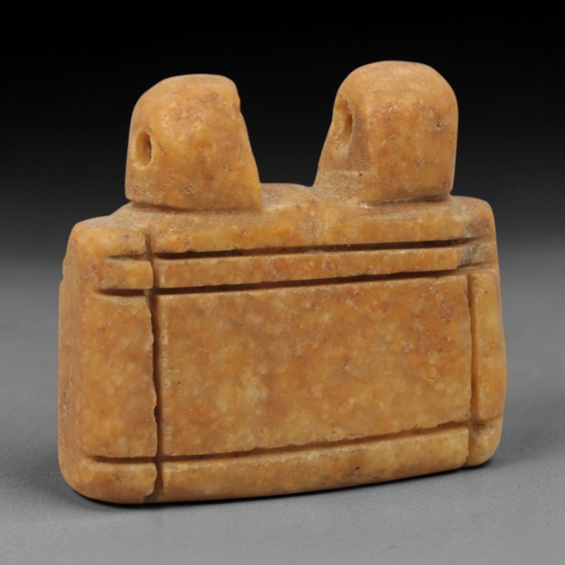 Ancient Stone Double Suspension Amulet - Near Eastern Pendant, 50XQ: Carved from a warm ochre stone, this amulet features a rectangular body incised with horizontal and vertical linear borders, topped by two perforated cylindrical projections for suspension. The form a