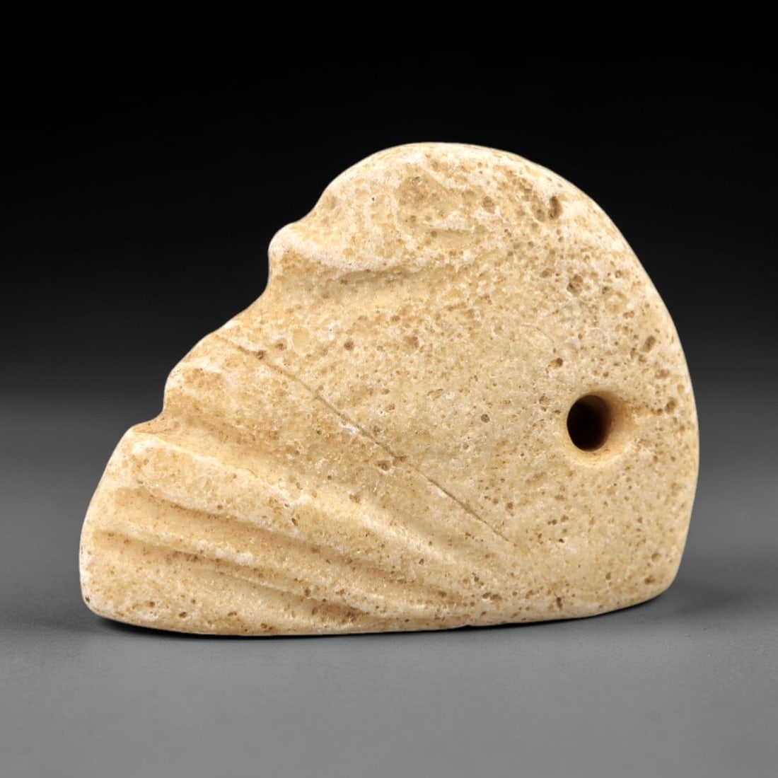Ancient Limestone Duck Amulet - Near Eastern Protective Talisman, 96AM: Carved from pale beige limestone, this 3x2cm duck amulet features a stylized avian form with incised linear details defining the wing feathers and simplified head profile. The stone retains a porous,