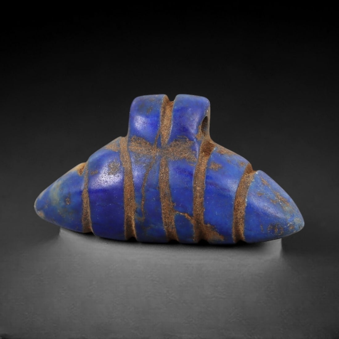 Ancient Lapis Lazuli Amulet - Egyptian Double Point Pendant, 17AP: Carved from lapis lazuli, this amulet features a symmetrical double-pointed form with a raised upper lug pierced for suspension, its body incised with vertical bands that define its segmented structur