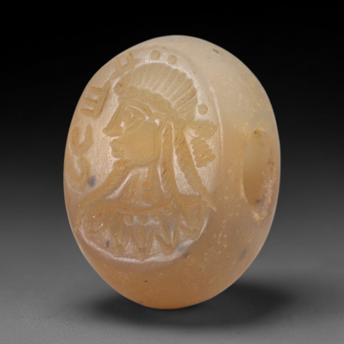 Ancient Chalcedony Stamp Seal - Sasanian Royal Bust, 58AK: Carved from translucent chalcedony, this oval Sasanian stamp seal features a central profile royal bust motif with a radiate headdress, braided hair, and ornate neck adornments, alongside incised epig