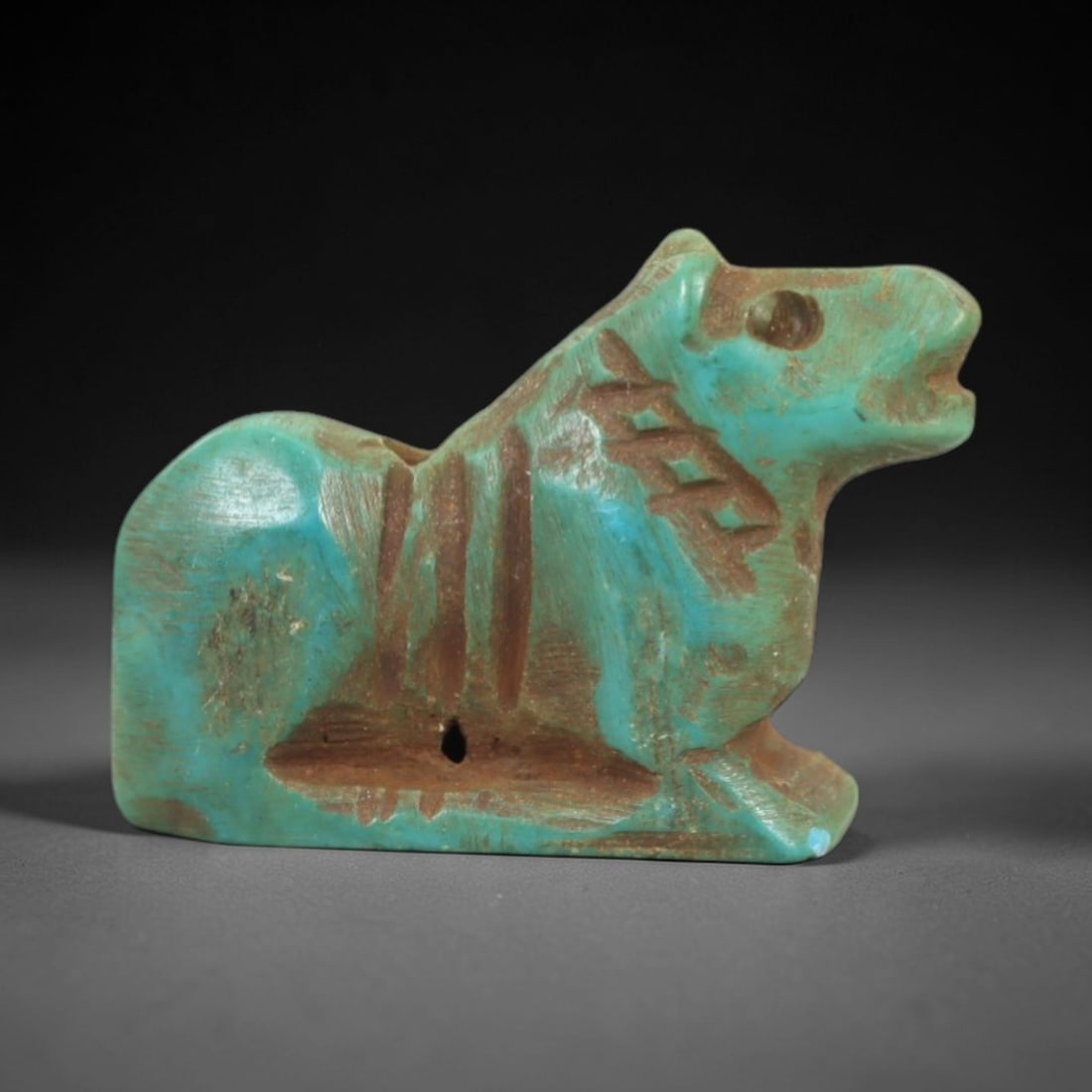 Ancient Turquoise Animal - Near Eastern Amulet Figurine, 78AK: Carved from polished turquoise, this amulet depicts a stylized recumbent animal with incised linear details defining the neck, torso, and facial features, including a defined eye and open mouth. Two s