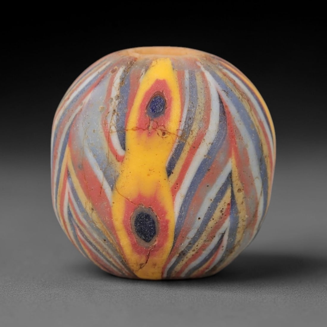 Ancient Glass Bead - Islamic Polychrome Trailed Sphere, 57ZM: This ancient bead is crafted from polychrome glass, formed using the trailed decorative technique characteristic of Islamic glassworking traditions. The spherical form features a dynamic pattern of sw