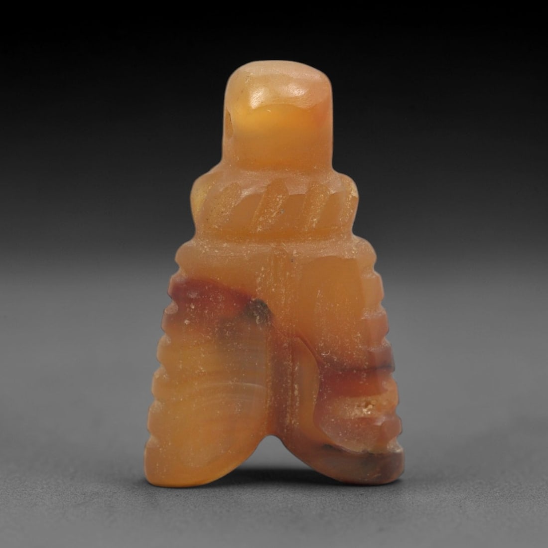 Ancient Carnelian Amulet - Egyptian Figurine, 83XS: This amulet is carved from warm amber-hued carnelian, featuring a stylized anthropomorphic or ritual form with a pierced suspension neck at the upper apex and vertically incised linear detailing along