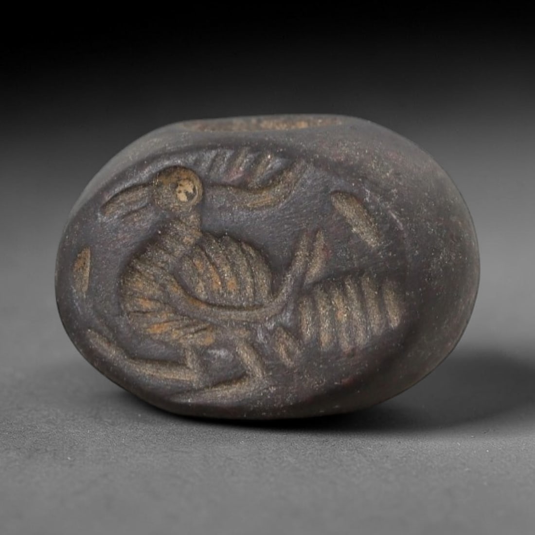 Ancient Stone Bird Stamp Seal - Near Eastern Amulet, 92AN: Carved from a dense, dark grey-brown stone, this oval stamp seal features a compact form with a central suspension hole, indicative of its function as a wearable amulet or personal seal. The flat face