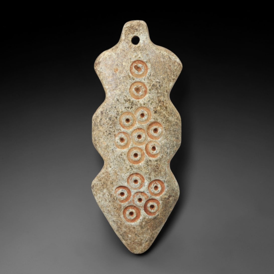 Ancient Steatite Amulet - Near Eastern Circular Motif Pendant, 2AL: Carved from steatite, this elongated, lobed amulet features three clusters of incised circular motifs (each with a central dot), arranged symmetrically across its surface, with a suspension hole at th