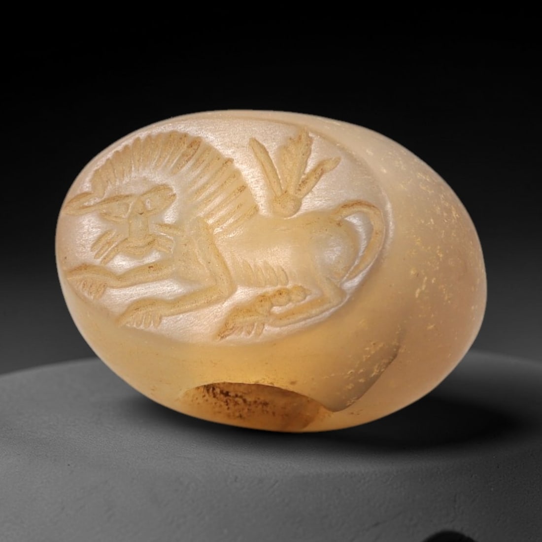Ancient Chalcedony Hemispherical Stamp Seal - Near Eastern Lion Amulet, 5AN: This ancient Near Eastern hemispherical stamp seal is carved from translucent, pale amber chalcedony, with a smooth, polished surface and subtle natural patina. The seal's oval face depicts a recumben