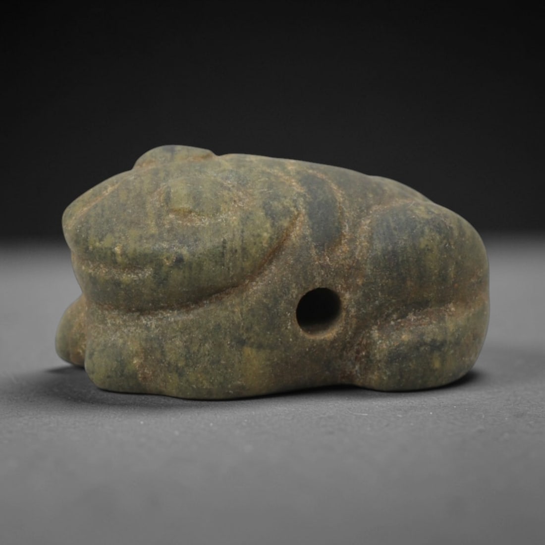 Ancient Stone Frog Amulet - Egyptian Animal Pendant, 34XQ: This amulet is carved from a mottled greenish-gray stone, shaped into a stylized crouching frog form with a perforated suspension hole through the body, confirming its use as a wearable protective cha