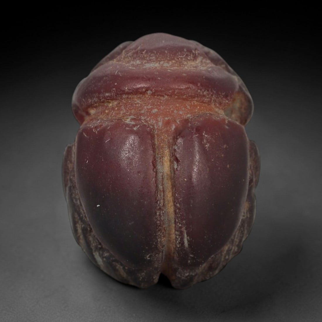 Ancient Carnelian Scarab Amulet - Egyptian Figurine, 34XS: Carved from rich, deep plum-red carnelian with natural tonal gradients and subtle mineral patination, this amulet is formed as a stylized scarab beetle with incised linear detailing to define the cent