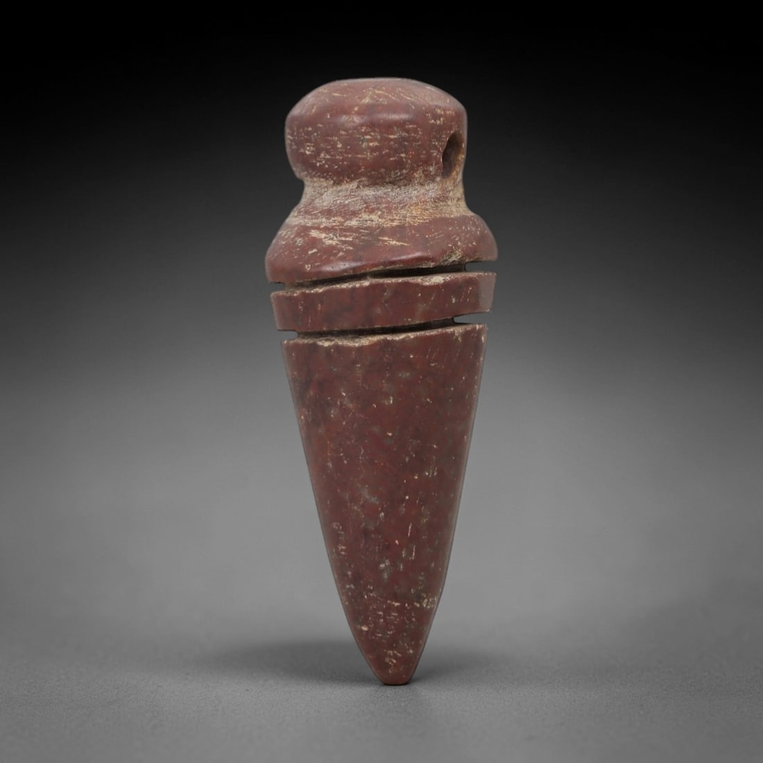 Ancient Egyptian Stone Amulet - Geometric Carved Pendant, 39AE: Carved from reddish-brown stone, this ancient Egyptian amulet features a tapering, elongated form with incised horizontal bands, a motif typical of Egyptian protective amulets. Craftsmanship is simple