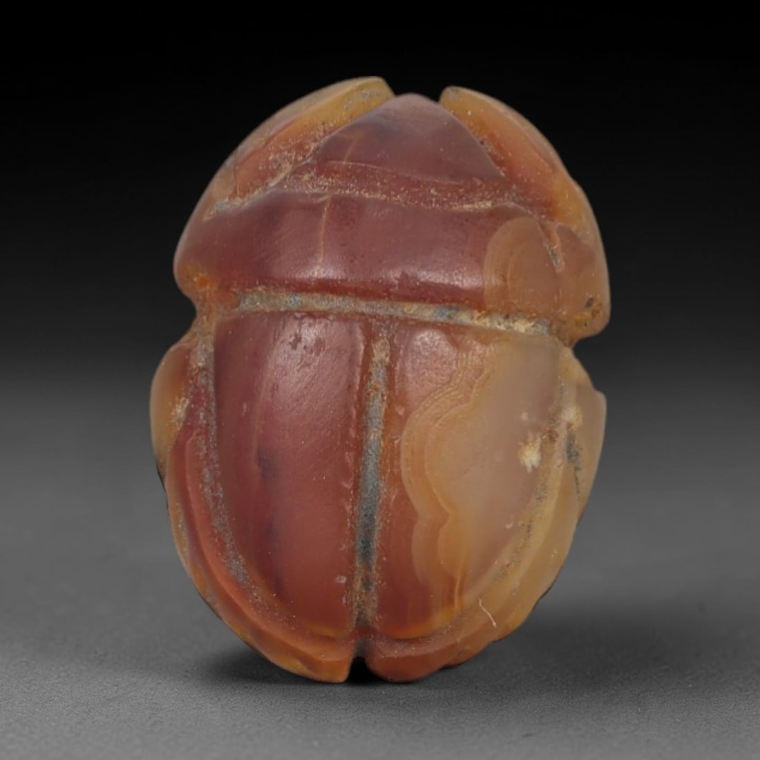 Ancient Banded Agate Scarab Amulet - Egyptian Figurine, 33AJ: Carved from striking banded agate with concentric layers of warm orange, deep red, and creamy white, this amulet is formed as a stylized scarab beetle with incised linear detailing to define segmented