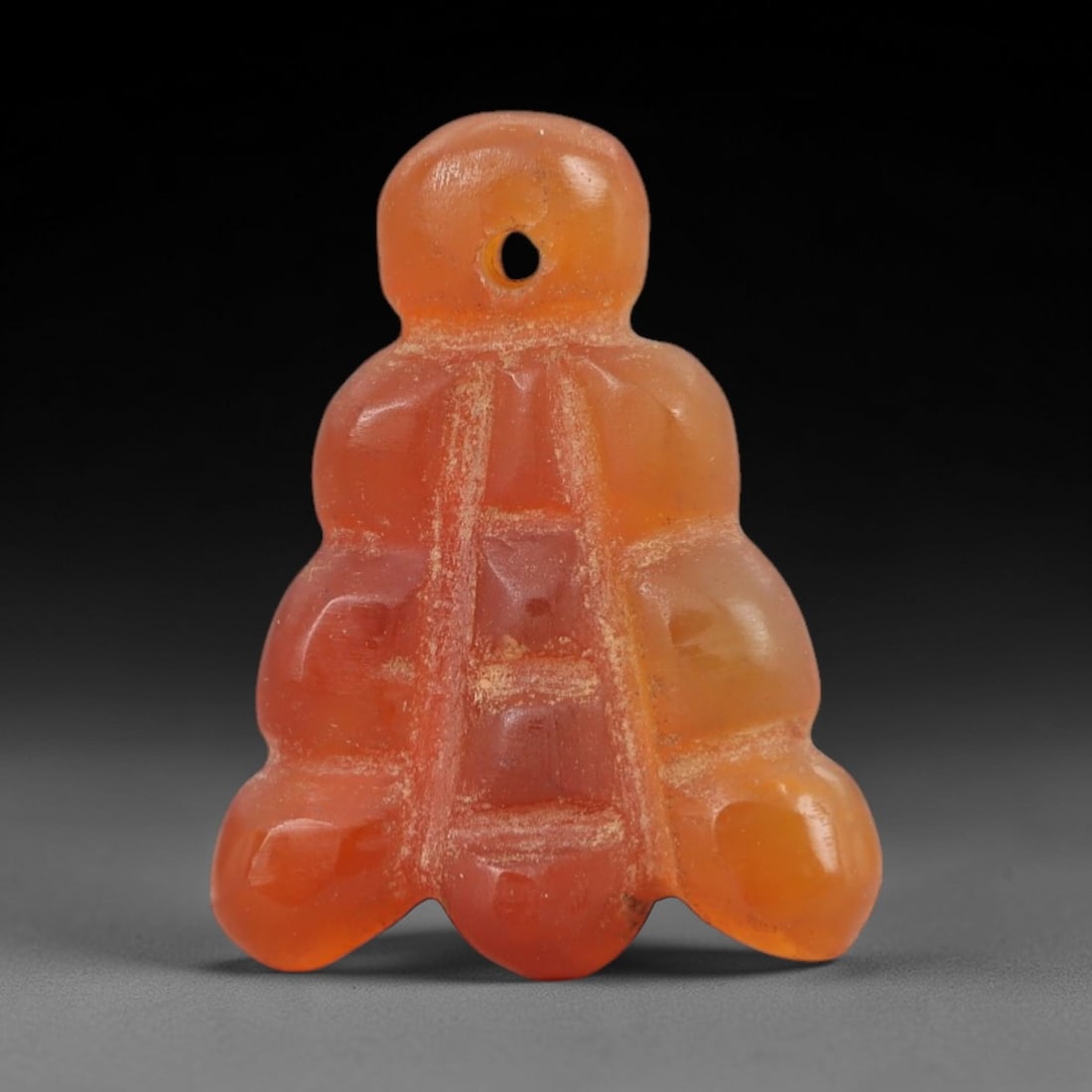 Ancient Carnelian Cluster Amulet - Near Eastern Figurine, 32AJ: Carved from translucent orange carnelian, this amulet is formed as a stylized clustered form with three vertical rows of rounded lobes, featuring incised linear detailing across the central axis to de