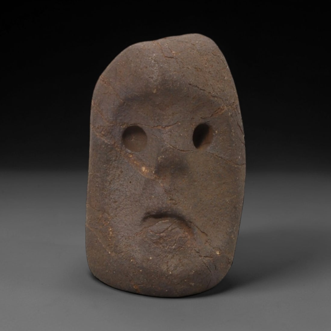 Ancient Stone Eye Idol - African Tribal Ritual Figurine, 80FW: Carved from a rough, dark brown stone with natural fissures, this artifact depicts a minimalist eye idol with two deeply pierced circular eye sockets, a simplified nasal ridge, and a recessed mouth, e
