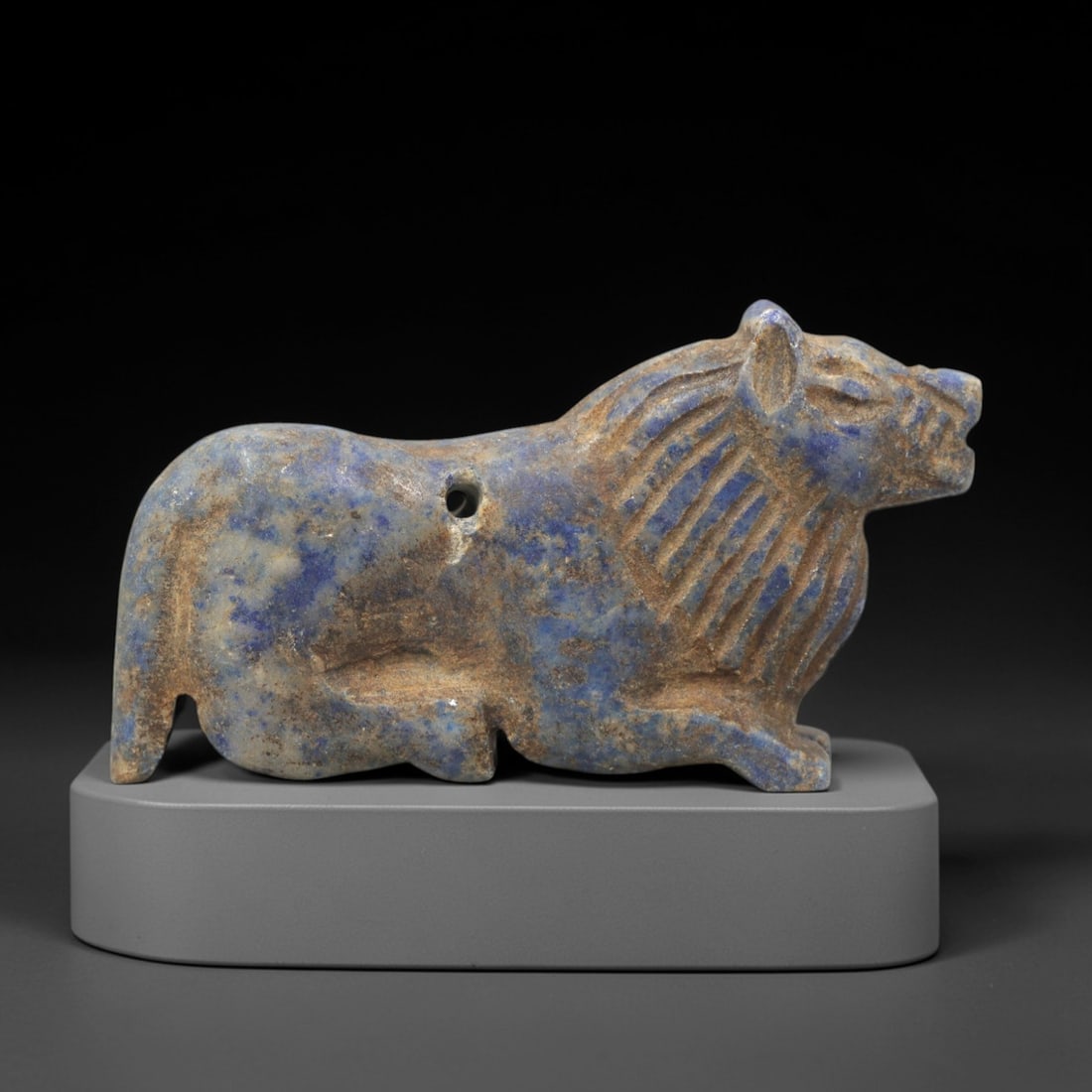 Ancient Lapis Feline Amulet - Near Eastern Figurine, 57XV: Carved from lapis lazuli, this amulet depicts a stylized feline in a recumbent posture, with incised linear striations defining the mane and simplified facial features including a defined snout and ea