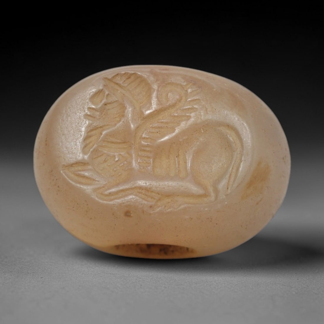 Ancient Chalcedony Stamp Seal - Near Eastern Winged Creature, 45ZS: Crafted from translucent chalcedony, this hemispherical stamp seal displays a deeply incised winged quadrupedal creature in profile, rendered with linear detailing to define its wings, body, and limbs