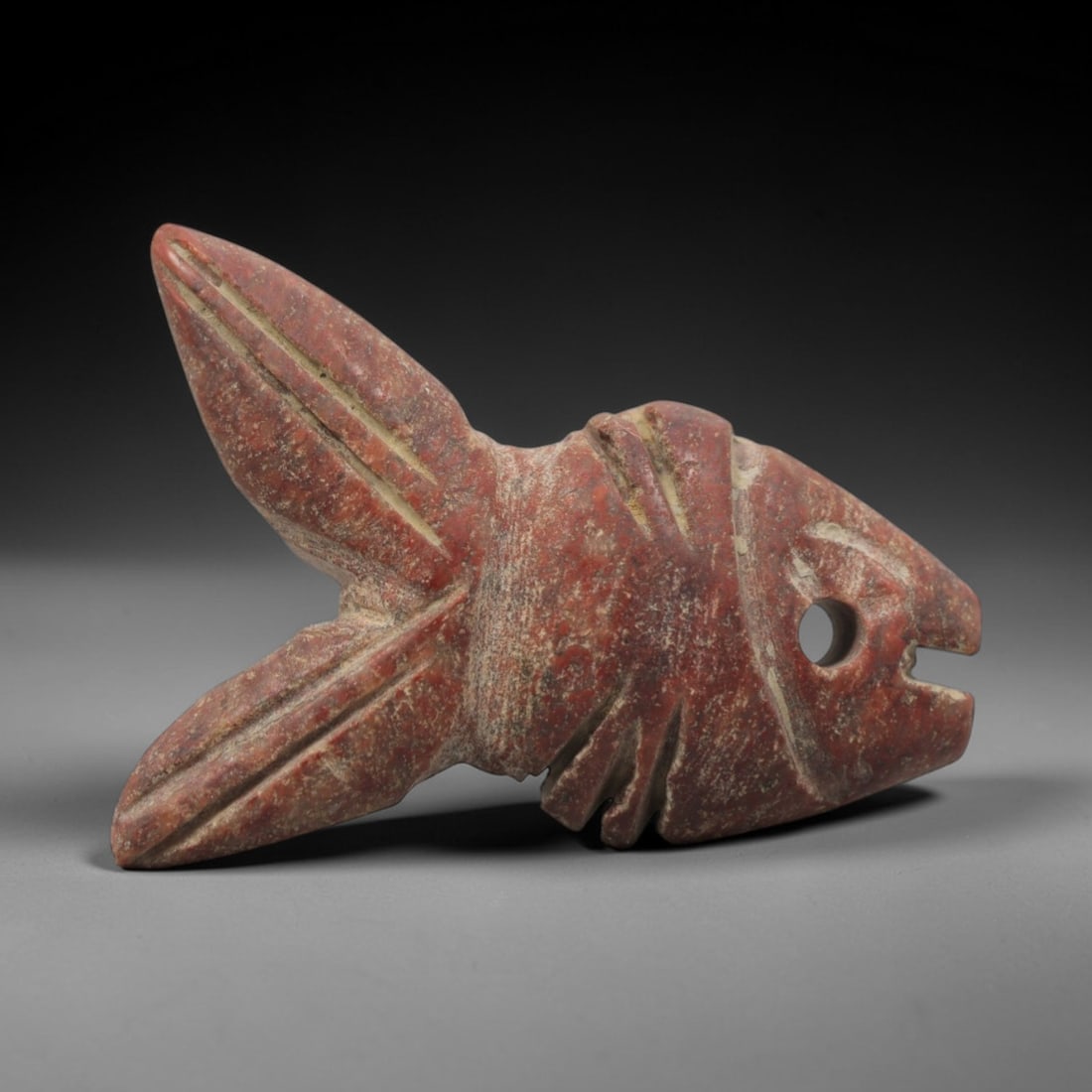 Ancient Egyptian Red Stone Fish Amulet - Carved Pendant Figure, 26ZV: This amulet is carved from a rich, deep red stone with natural mineral speckling and patination, likely brecciated jasper or red steatite, featuring a stylized fish form. The piece displays a streamli
