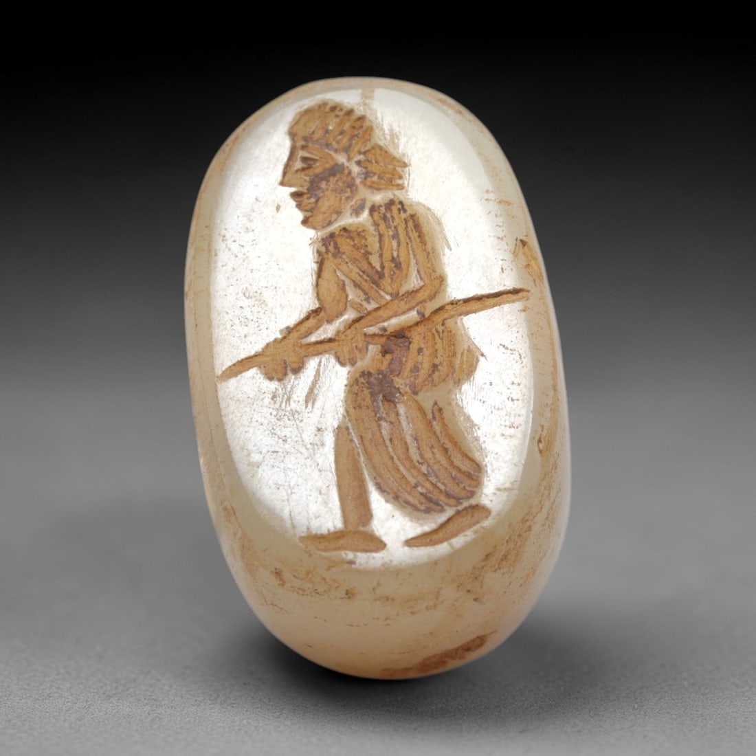 Ancient Chalcedony Stamp Seal - Near Eastern Warrior Figure, 58ZS: Crafted from translucent chalcedony, this oval stamp seal bears an incised profile of a striding warrior figure, rendered with linear detailing to define his headdress, draped garment, and the spear h