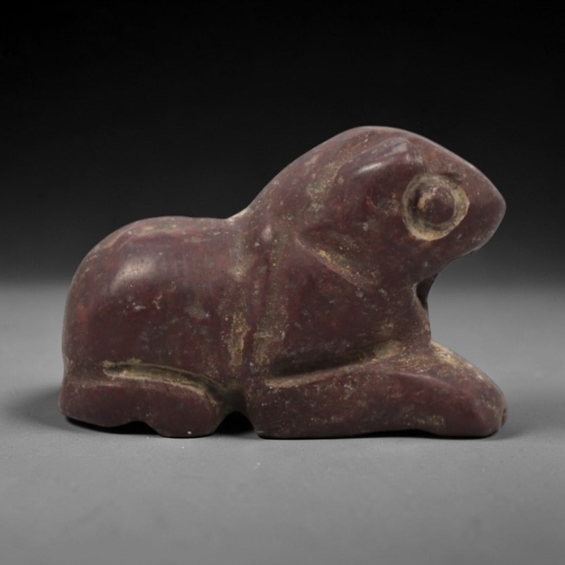 Ancient Near Eastern Stone Hare Amulet - Carved Figurine, 24ZV: This amulet is carved from a dense, reddish-brown stone, likely hematite or a similar iron-rich sedimentary rock, with subtle incised details defining its recumbent hare form. The piece depicts a hare