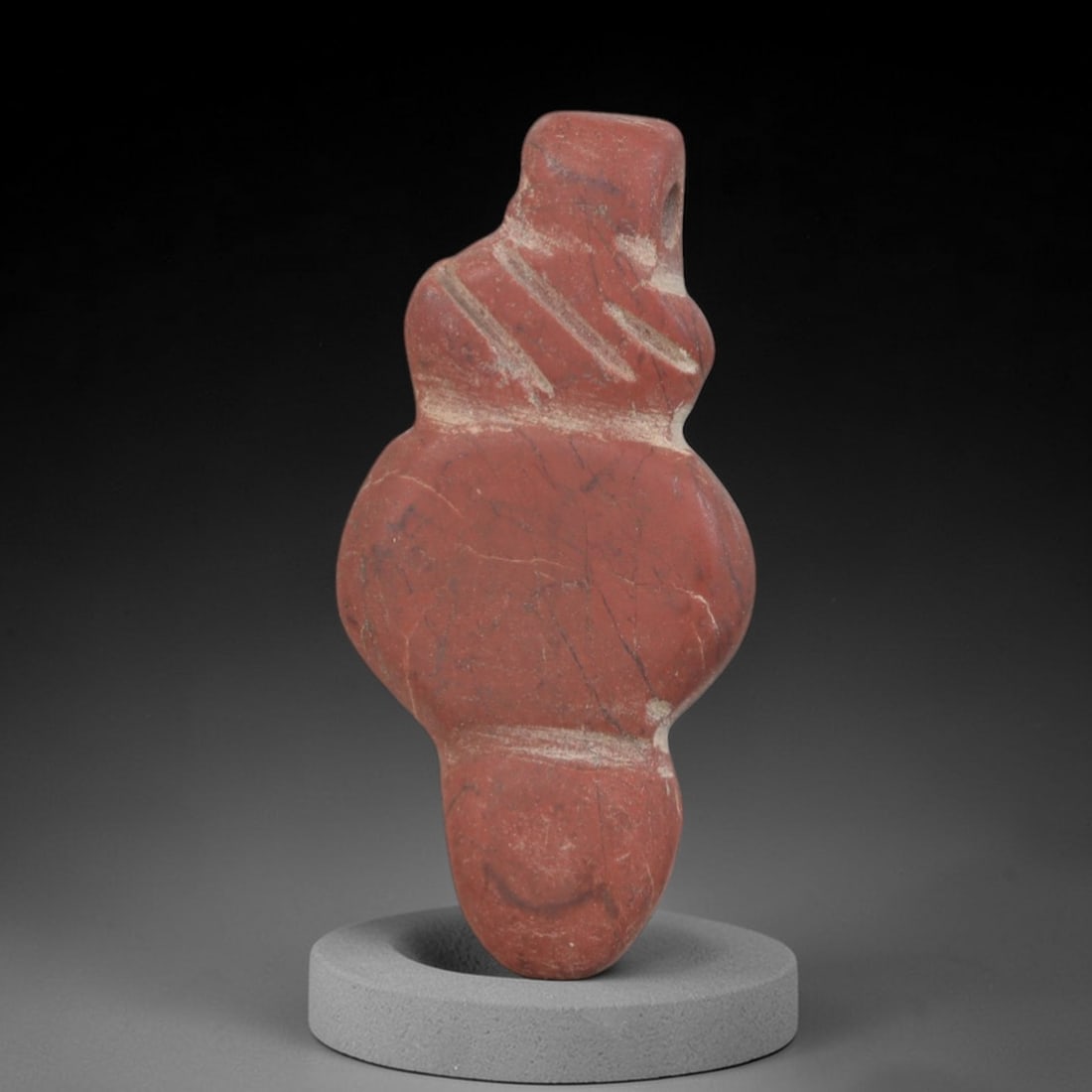 Ancient Stone Amulet - Near Eastern Figurine, 88AP: This artifact is carved from red stone with a naturally weathered surface and subtle patina, exhibiting faint mineral veining consistent with ancient Near Eastern craftsmanship. The form is stylized a