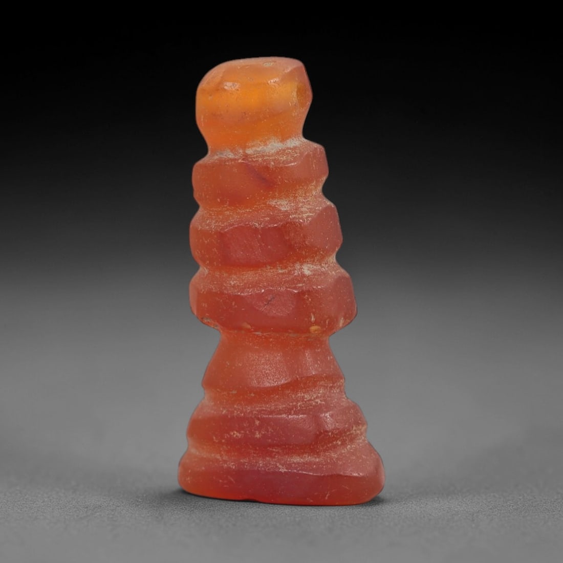 Ancient Carnelian Djed Amulet - Egyptian Figurine, 53AJ: Carved from vibrant orange carnelian, this amulet is formed as a stylized djed pillar, featuring stacked horizontal ringed segments and a flared base, consistent with ancient Egyptian funerary amulet