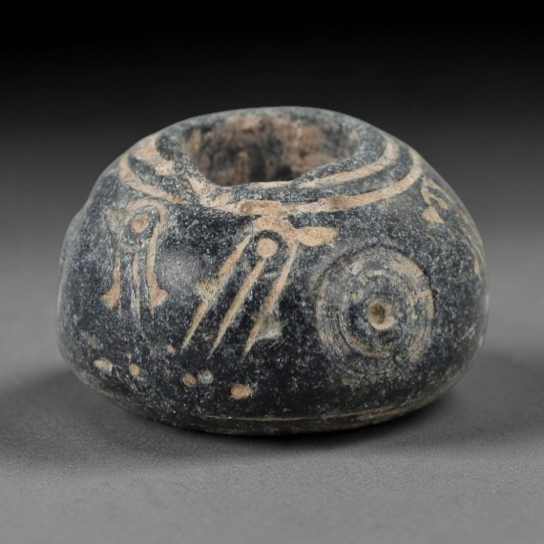 Ancient Bone Spindle Whorl - Near Eastern Avian Motif, 81AH: This ancient Near Eastern spindle whorl is carved from bone, featuring a biconvex form with a central perforation. The surface is incised with avian and linear motifs, a common decorative technique on
