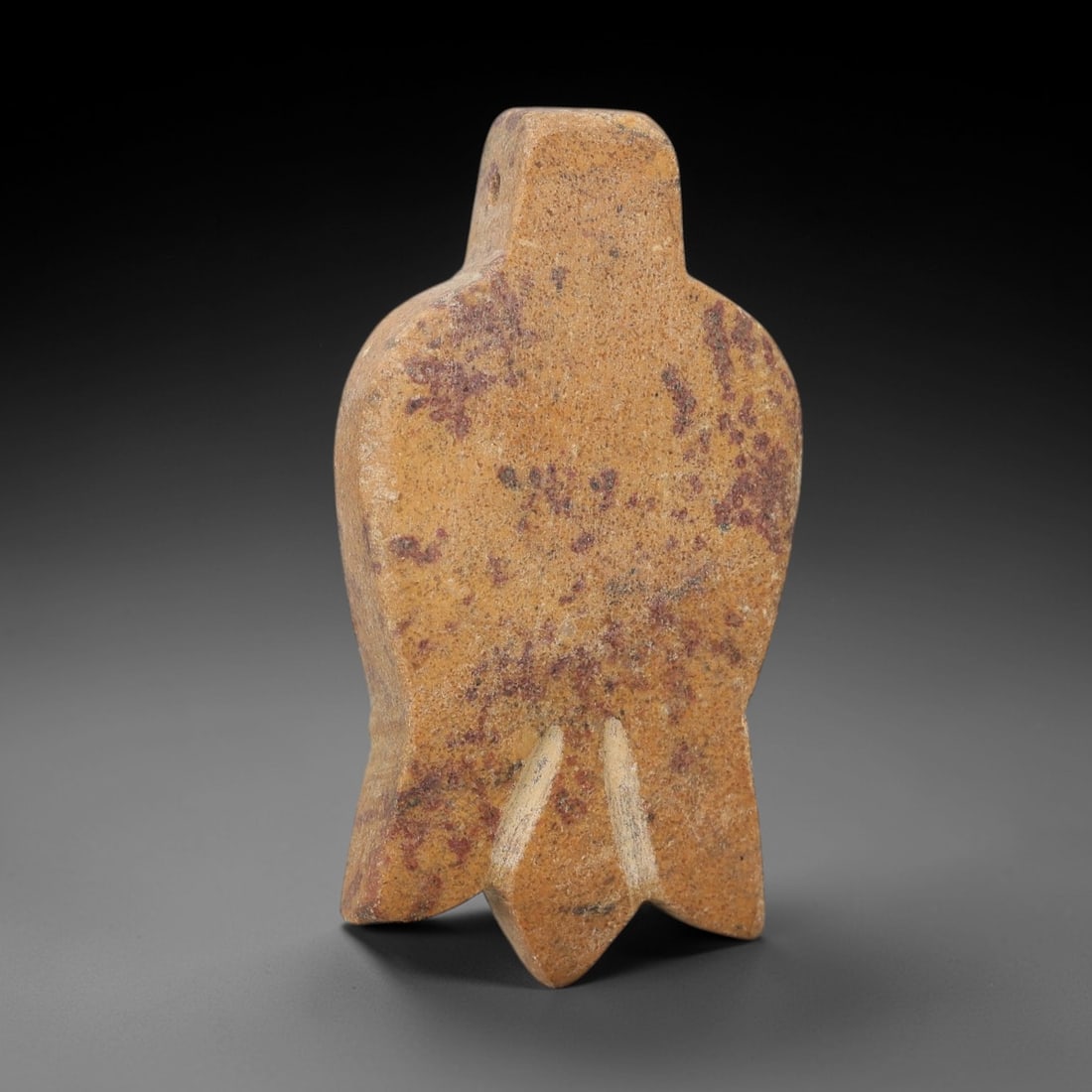 Ancient Stone Bird Amulet - Egyptian Ritual Figurine, 18AG: This amulet is carved from a single piece of tan stone, exhibiting a granular texture with scattered reddish-purple mineral inclusions across its surface. The form is schematically rendered as a bird,