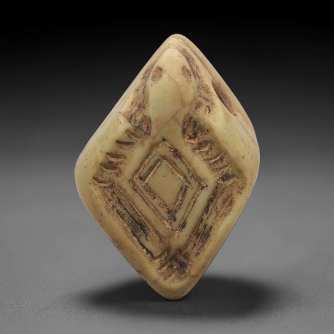 Ancient Serpent-Head Amulet Bead - Near Eastern Protective Artifact, 14ZR: This artifact is a diamond-shaped amulet bead, executed in the stylized zoomorphic tradition of the ancient Near East. The upper portion is carved into a serpent (snake) head, while the main face feat