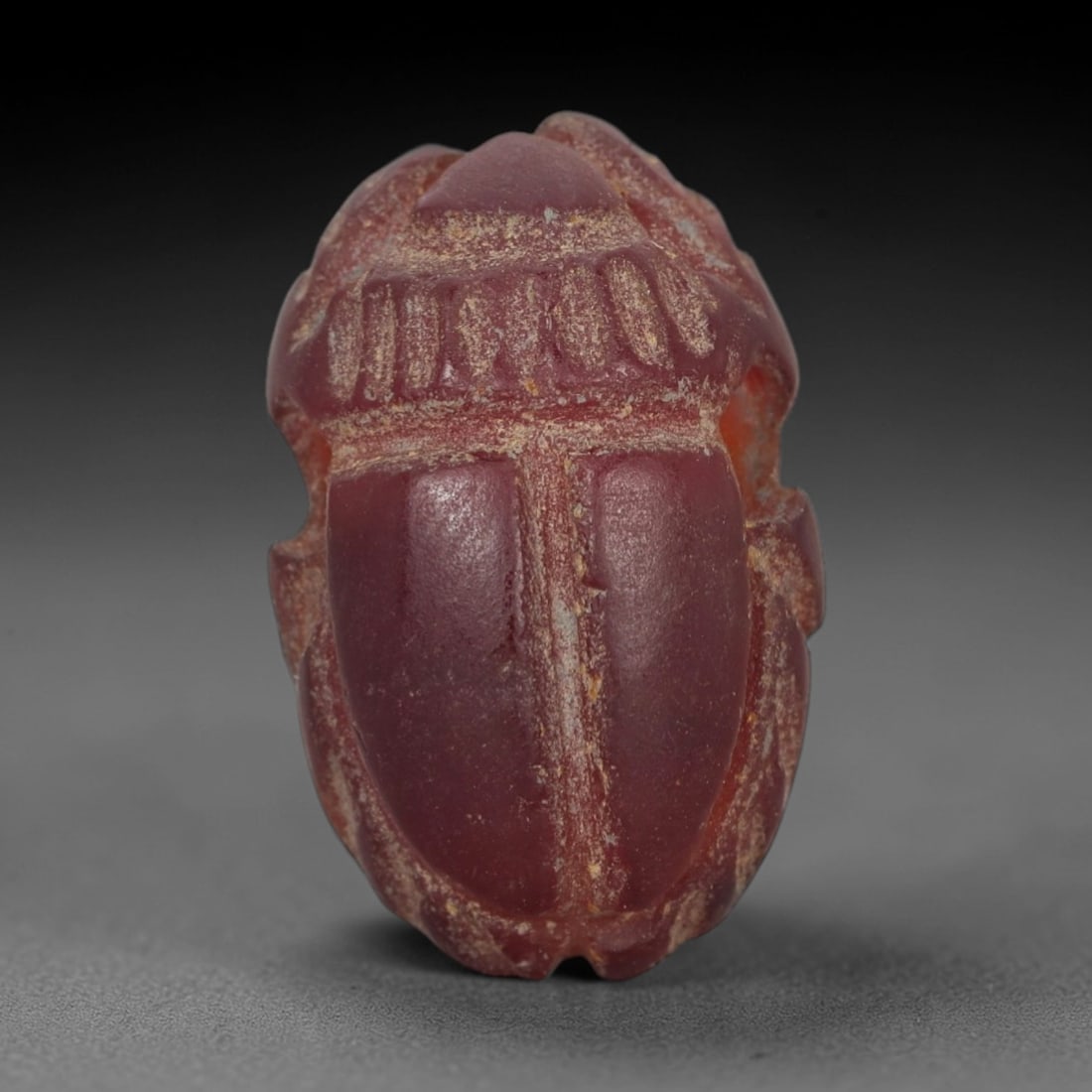 Ancient Carnelian Scarab Amulet - Egyptian Figurine, 30XS: Carved from rich, deep rose-red carnelian with subtle amber undertones and natural mineral patination, this amulet is formed as a stylized scarab beetle with incised linear detailing to define the cen