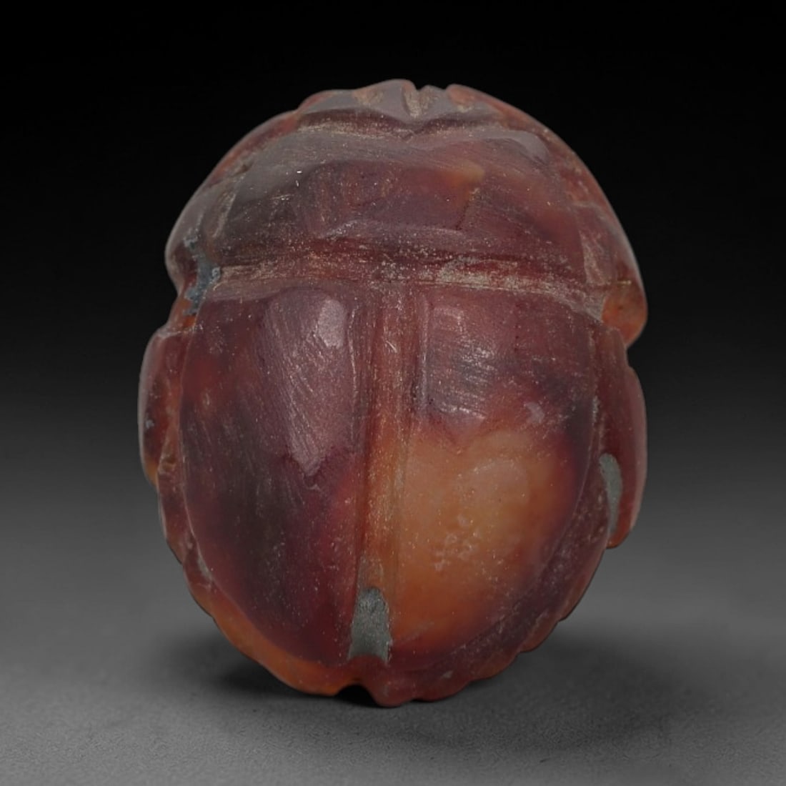 Ancient Carnelian Scarab Amulet - Egyptian Figurine, 18AJ: Carved from rich, deep red carnelian with natural amber-orange gradients, this amulet is formed as a stylized scarab beetle with incised linear detailing to define segmented head plates, central body