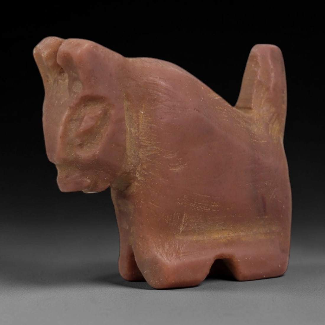 Ancient Reddish Stone Zoomorphic Amulet - Near Eastern Figurine, 84AD: Carved from warm reddish stone with fine granular texture, this amulet depicts a stylized zoomorphic form in a compact, upright posture. The creature features simplified facial details, angular body c