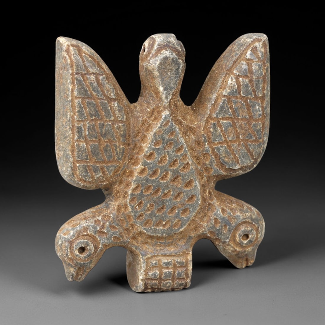 Ancient Stone Zoomorphic Amulet - Near Eastern Bird Figure, 21AM: This amulet is carved from dark stone, depicting a composite zoomorphic form with a central bird body, outstretched wings, and dual bird heads at the base, rendered in raised relief with incised geome