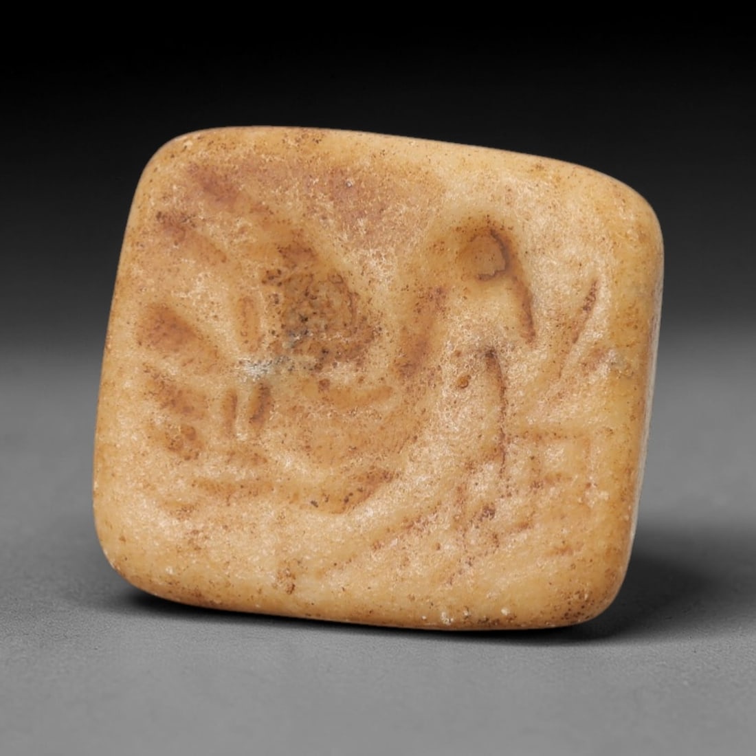 An Ancient Steatite Stamp Seal, 20th Century, 65FW: Carved from light tan steatite with a naturally aged, patinated surface and subtle brown inclusions, the stamp seal is trapezoidal in form, with a flat base and a conical top pierced for suspension. T