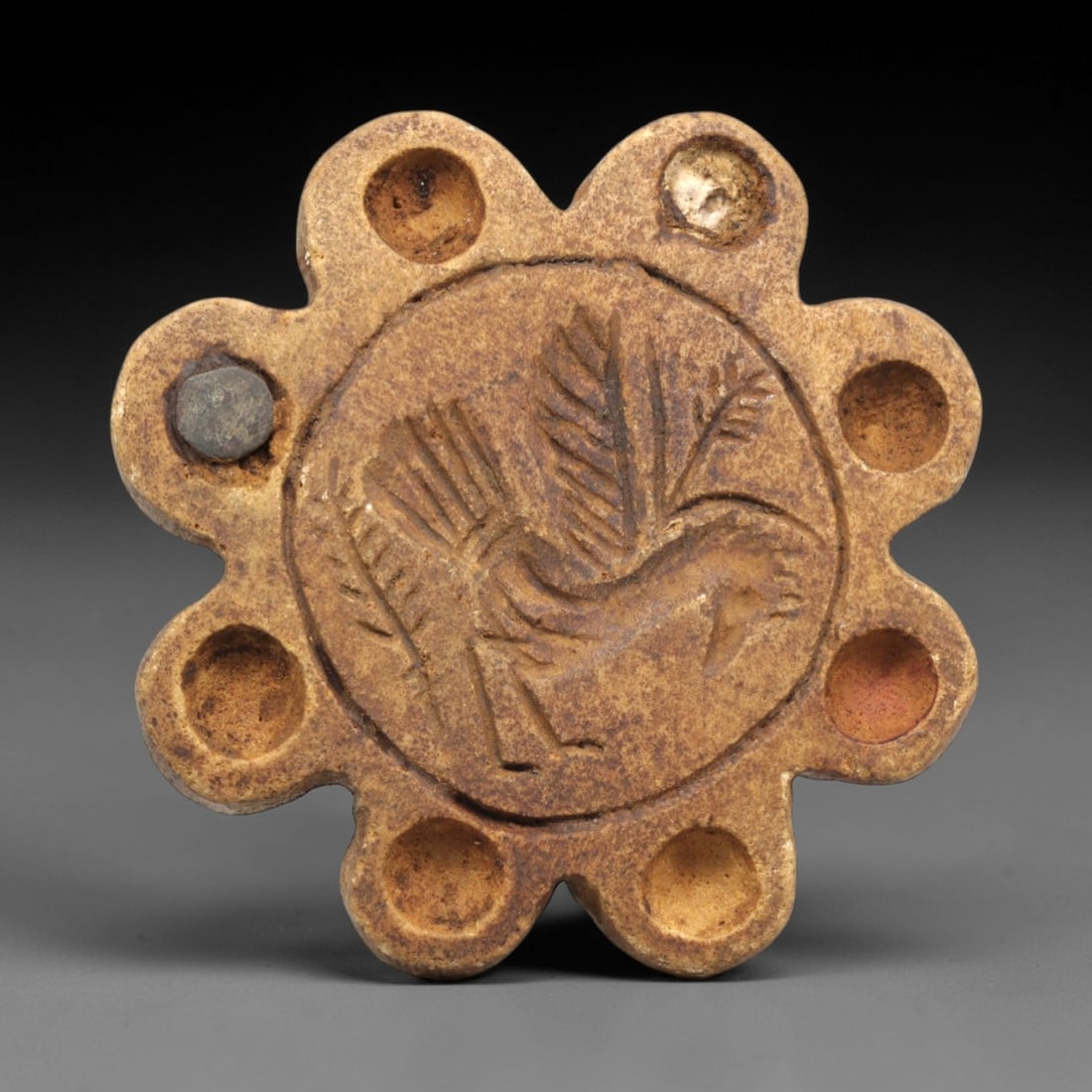 Ancient Steatite Stamp Seal - Near Eastern Bird Motif, 81ZP: This lobed stamp seal is carved from steatite, featuring a central medallion incised with a striding bird motif, detailed with feathered wings and a stylized beak, surrounded by eight evenly spaced ci