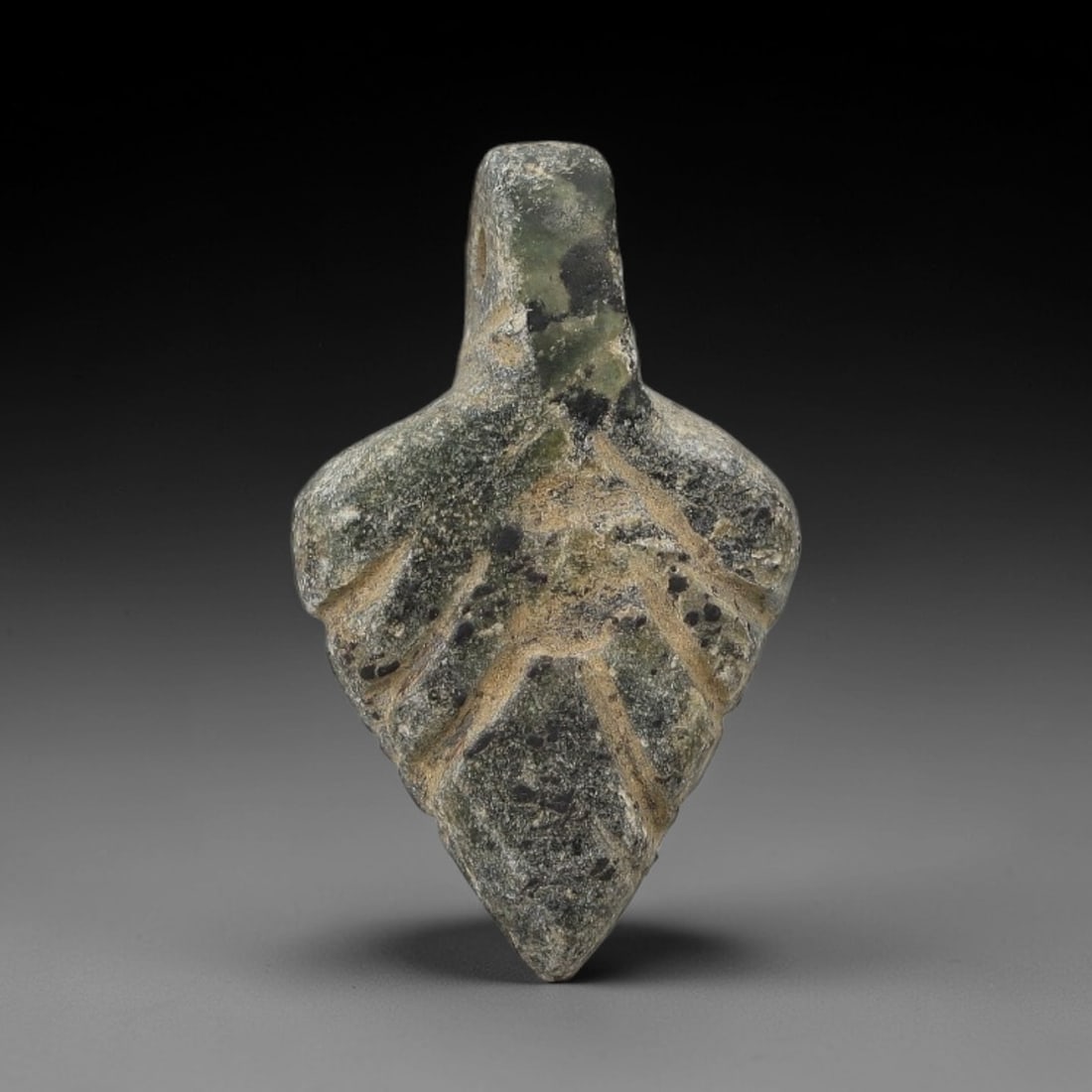Ancient Stone Leaf Amulet - Near Eastern Ritual Figurine, 51AG: This amulet is carved from a single piece of mottled green stone, exhibiting a granular texture with subtle ochre patina and dark mineral inclusions across its surface. The form is stylized as a leaf,