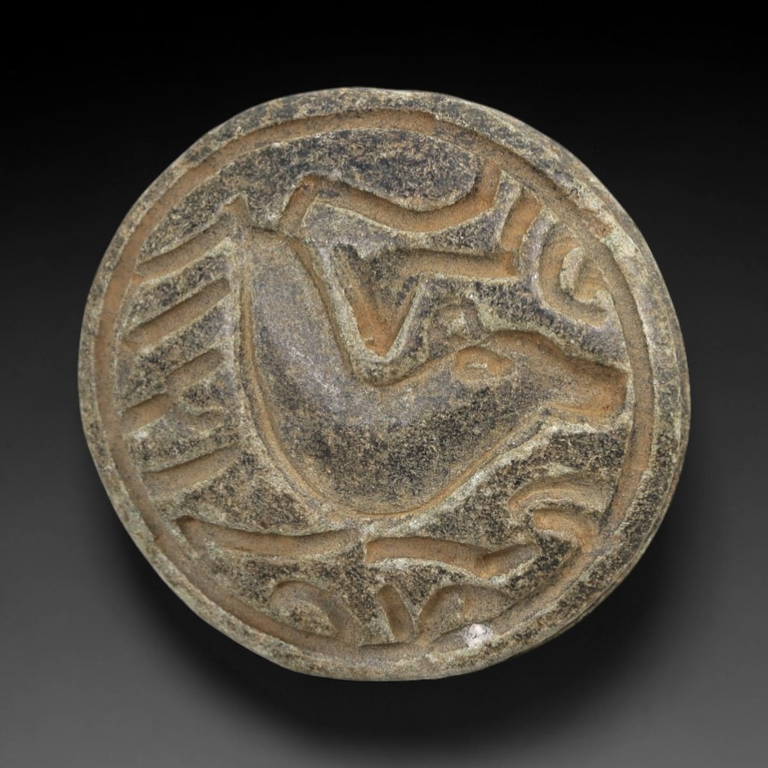 Ancient Stone Animal Amulet - Near Eastern Bead Pendant, 4AM: This double convex bead amulet is carved from a weathered, granular stone with a mottled, earthy patina indicative of long-term burial exposure. The central relief depicts a stylized horned animal, li
